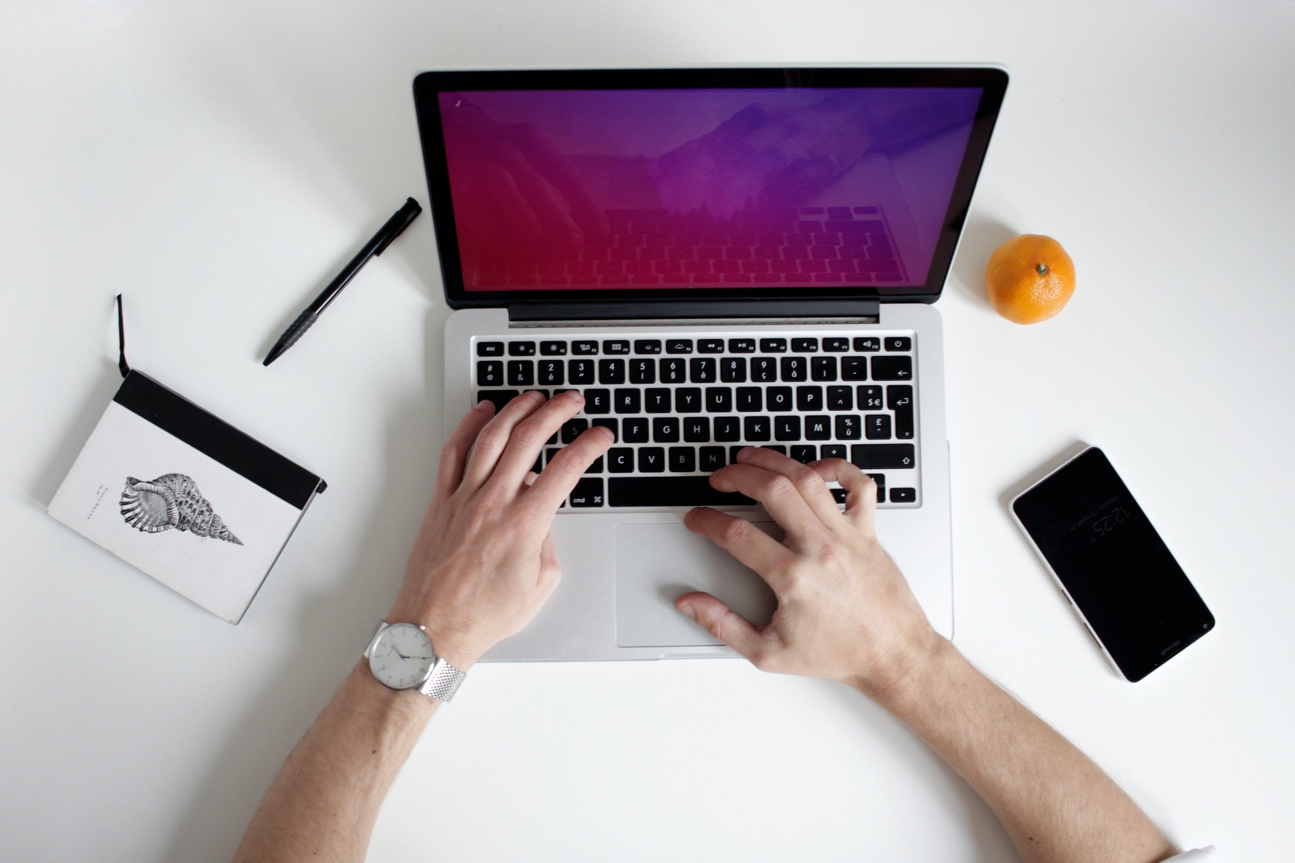 Hände tippen auf Laptop-Tastatur neben Smartphone auf einem aufgeräumten Schreibtisch