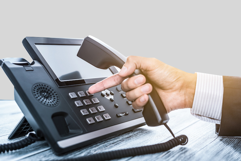 Hand wählt eine Nummer an einem modernen Bürotelefon